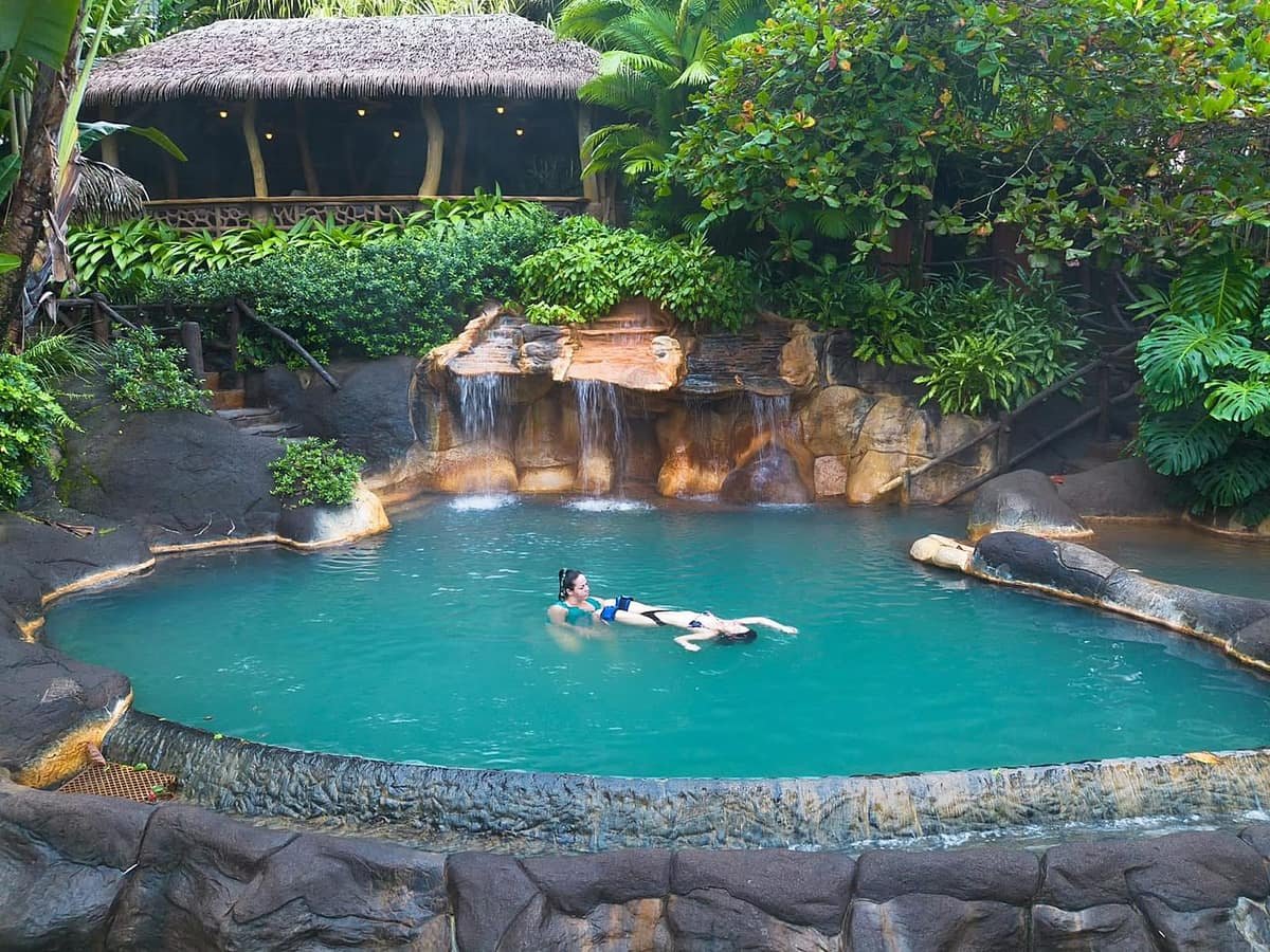 Sesión de Janzu en una piscina termal turquesa con cascada y un rancho de techo de palma